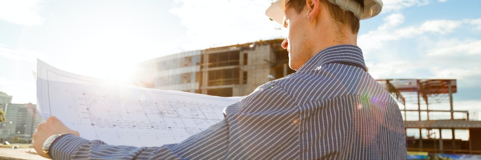 Architect in helmet with blueprints looks at camera in a building site